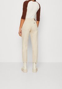 Béžové kalhoty s vysokým pasem, bočními kapsami, zúženými nohavicemi a ohrnutým lemem. Kombinováno s topem s raglánovými rukávy v hnědé a bílé barvě.