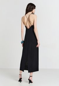 Schwarzes Maxikleid mit einem tiefen V-Ausschnitt am Rücken, dünnen überkreuzten Trägern und einem seitlichen Schlitz. Glattes Material und Saum auf Knöchelhöhe.