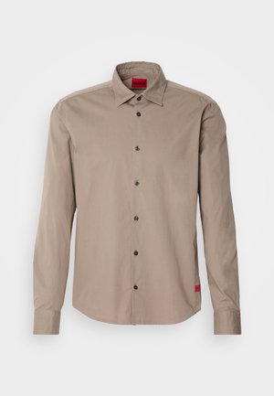 Long-sleeve shirt in light brown cotton with a button-down collar, black buttons, and a small red logo tag at the hem.
