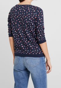 Suéter azul marino con patrón floral multicolor, puños y dobladillo acanalados, hecho de una tela suave. Combinado con unos jeans de corte relajado.