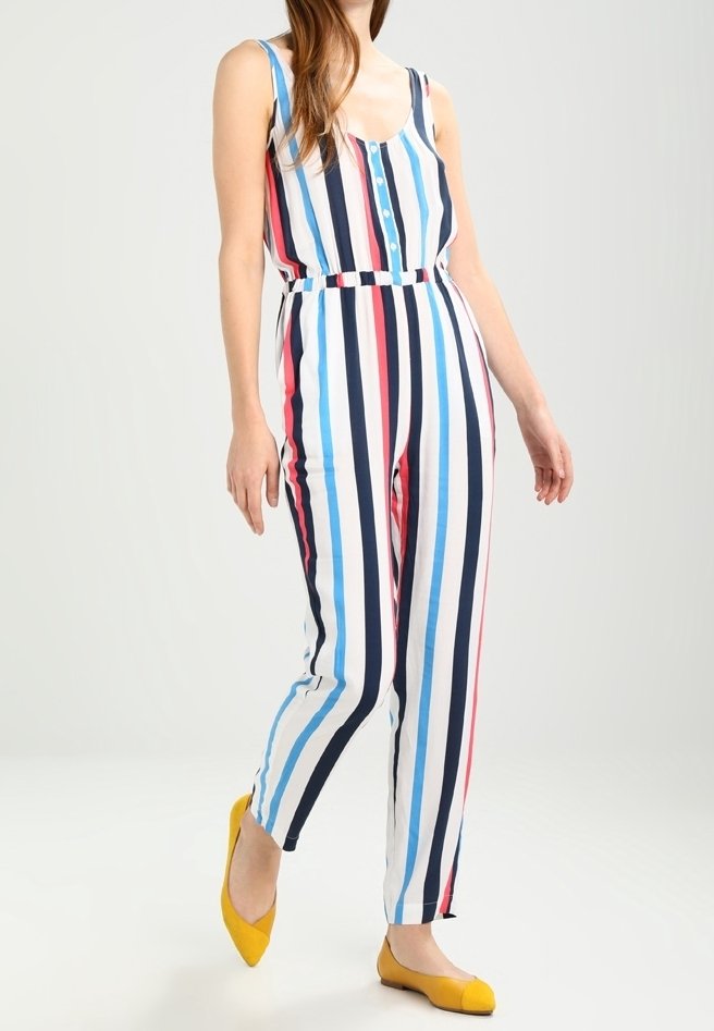Randig jumpsuit med vertikala ränder i blått, rött och marinblått, med knäppning fram och åtsittande midja. Matchad med gula lägenheter.