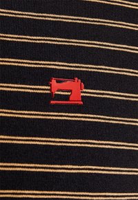 Gestreifter Strickstoff mit schwarzen und goldenen horizontalen Linien; zeigt ein kleines rotes Nähmaschinen-Graphic. Weicher Stoff und lässiges Design.