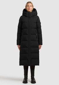 Manteau long matelassé noir avec capuche, doté d'une fermeture éclair, de coutures verticales et de deux poches latérales. Tissu texturé avec une finition lisse.