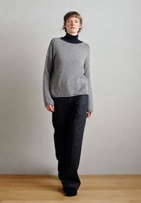 Szary wełniany sweter o luźnym kroju i długich rękawach zestawiony z czarnymi dżinsami o szerokich nogawkach. Miękka faktura, minimalistyczny design, bez widocznych wzorów.