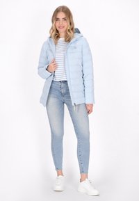 Ljusblå puffjacka med huva, dragkedja och quiltat mönster, i kombination med en randig skjorta och ljusa denimjeans. Vita sneakers fulländar stilen.