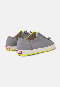Gray canvas sneakers with white soles and yellow accents. Features round toe, laces, and red logo on the heel. Casual design.