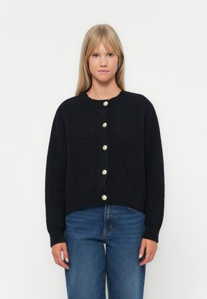 Cardigan nero lavorato a maglia con un motivo testurizzato, dotato di scollatura tonda e grandi bottoni dorati lungo la parte anteriore. Vestibilità corta.