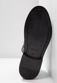 Suela de zapato de cuero negro con diseño texturizado, tacón plano y marca en relieve. Acabado suave y construcción robusta. Diseñado en Portugal.