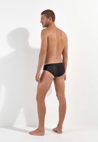 Schwarze Badeslips für Herren aus glattem Material, mit niedrigem Bund und schlichtem Design. Minimale Nähte und eine figurbetonte Silhouette.