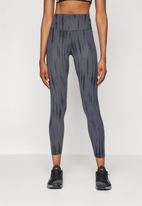 Leggings grises con un patrón de rayas verticales, cintura alta y textura suave. Llevados con zapatillas deportivas negras.