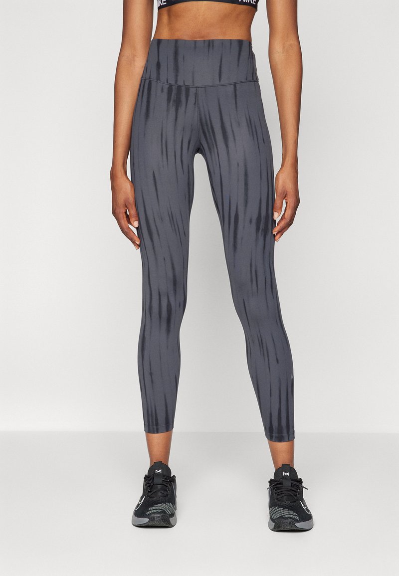 Leggings grises con un patrón de rayas verticales, cintura alta y textura suave. Llevados con zapatillas deportivas negras.