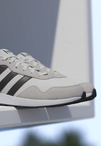 Paire de baskets Adidas blanches et grises avec des bandes noires reposant sur un rebord blanc contre un arrière-plan extérieur flou.