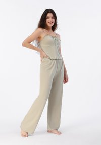 Mono verde claro con un top ajustado, tirantes finos y una cintura con volantes, pantalones de pierna ancha que fluyen y una textura suave.
