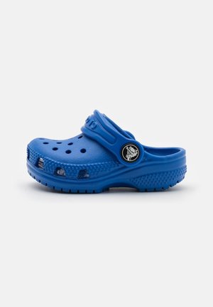 Blue plastic clog with ventilation holes, a back strap, and textured sole. Features a round logo accent on the side.