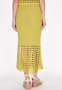 Stickad maxikjol i olivgrön med ribbad textur och öppen virkning vid fållen. Kombinerad med beige espadrillosandaler med remmar.