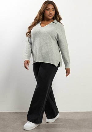 Lichtgrijze, gebreide trui met een v-hals en een kraag, gecombineerd met zwarte wijde broek en witte sneakers, wat een casual uitstraling benadrukt.