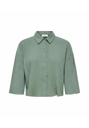 Camicia verde con bottoni realizzata in tessuto testurizzato. Presenta un colletto e maniche a 3/4. Il tessuto ha un aspetto trapuntato.