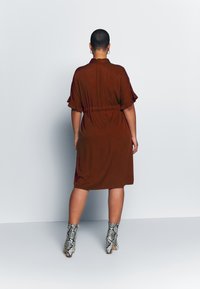 Abito marrone fino al ginocchio con maniche a volant e vita con cintura. Abbinato a stivali con tacco alto in pelle di serpente con texture.