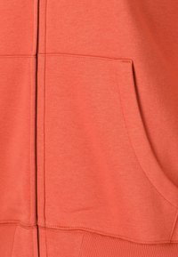 Koraal kleurige rits hoodie gemaakt van een zachte katoenmix, voorzien van een kangoeroezak, ribgebreide manchetten en een gladde textuur met zichtbare stikseldetails.