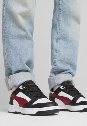 Mustat ja valkoiset tennarit punaisilla yksityiskohdilla, joissa on sileä nahkapinta, pyöreä varvas ja kumipohja. Yhdistetty vaaleansinisien käännettyjen farkkujen kanssa.