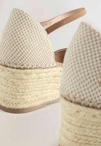 Sandali espadrilles beige intrecciati con una piattaforma in juta intrecciata e una cinturino alla caviglia liscio. La tomaia presenta un motivo a scacchi testurizzato.