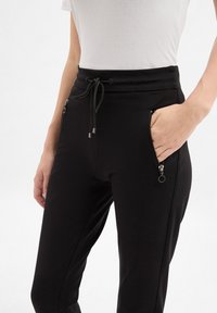 Schwarze Jogginghosen aus weichem Stoff, mit einem Kordelzugbund, Reißverschlusstaschen und einer schmalen Passform mit seitlichen Nähten.