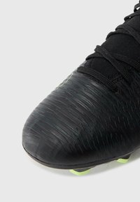 Botas de fútbol negras con superficie texturizada y acentos verdes. Presentan una puntera redondeada, un cordón seguro y una suela duradera con tracción de tacos.