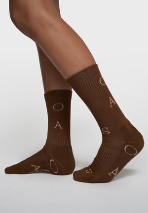 Braune Stricksocken mit gerippter Struktur und kontrastierenden hellen Buchstaben. Knöchellang mit Logodetail an den Seiten.