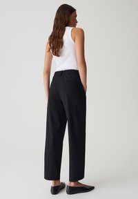 Pantalons larges noirs à taille haute, dotés d'une ceinture élastique et de deux poches arrière, associés à un débardeur blanc ajusté.
