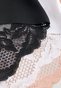 Czarna koronkowa lamówka z kwiatowym wzorem, ułożona warstwowo na białej i brzoskwiniowej koronce, prezentująca misternie wykonane detale i faliste krawędzie. Widoczna jest gładka czarna tkanina.