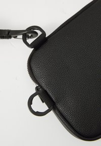 Black textured leather pouch with a smooth zip, featuring metal clips and a textured surface for grip, suitable for carrying small items.