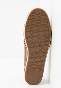 Semelle d'une chaussure marron avec une bande de roulement en caoutchouc texturée présentant un motif répétitif "MK" et un grip rectangulaire au talon.
