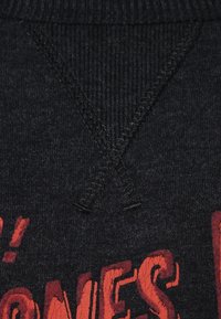 Fellone grigio scuro con un motivo ricamato rosso testurizzato. Presenta un collo a V per un tocco di dettaglio in più.