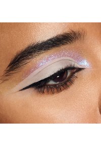 Ingrandimento di un occhio chiuso con ombretto lavanda glitterato, eyeliner nero a virgola ben definito e sopracciglio scuro ben curato su un tono di pelle caldo.