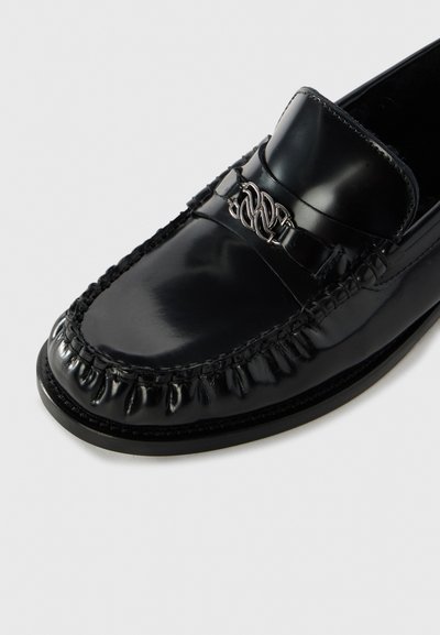 Schwarze Lederloafer mit glänzender Oberfläche, ausgestattet mit einem geflochtenen Steppmuster und einem dekorativen silbernen Metallakzent auf dem Obermaterial.