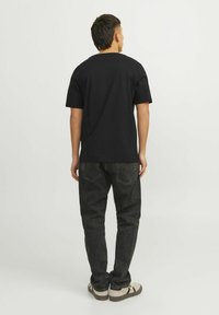 Sort kortærmet t-shirt med en afslappet pasform, parret med mørke jeans. Synlig syning og detaljer ved baghalsudskæringen. Flad stofstruktur.