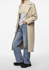 Beżowy długi płaszcz z wełny, sweter w paski, jasnoniebieskie dżinsy oraz czarne buty na grubej podeszwie, charakteryzujące się luźnym krojem i szerokimi nogawkami.