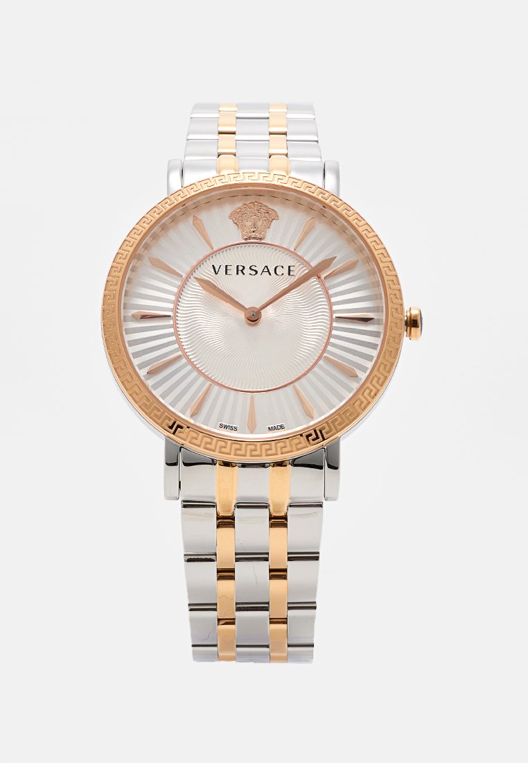 Montre Versace avec un bracelet en métal argenté et doré, un cadran rond à lunette dorée, un cadran blanc texturé et des index horaires en chiffres romains.