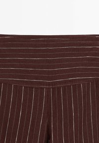 Burgundiska byxor med vita vertikala ränder, med en bred midja och sydda sömmar, tillverkade av ett texturerat tyg.