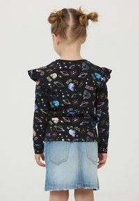 Czarny top z długim rękawem z kolorowym nadrukiem w tematyce kosmicznej. Posiada falbany na ramionach i jest zestawiony z jasnoniebieską spódnicą dżinsową.