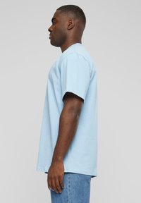 T-shirt en coton bleu clair au fit décontracté, à manches courtes et col rond. Le tissu a une texture lisse, porté avec un jean en denim bleu.