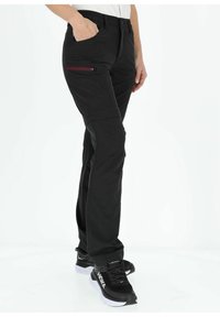 Black athletic pants with a fitted design, elastic waistband, zippered pocket in maroon, and flat seam detailing, paired with black sneakers.