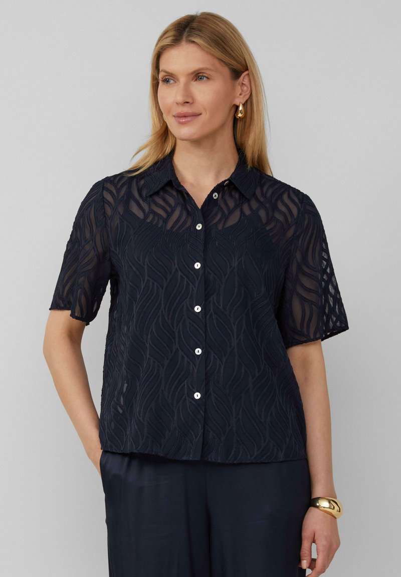 Marineblauwe short-sleeve shirt met een textuurpatroon van golven, knoopsluiting en een klassieke kraag. De stof lijkt lichtgewicht en semi-doorschijnend.