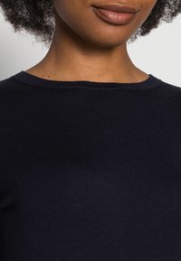 Navyblaues Strickoberteil mit rundem Halsausschnitt und gerippter Textur, aus glattem Stoff und mit figurbetonendem Design am Kragen.