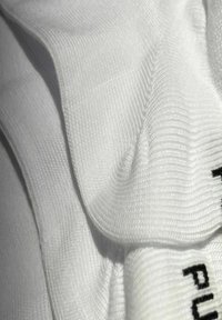 Weiße Baumwollsocken mit geripptem Muster und glatter Oberfläche, die schwarze Schrift auf dem Abschluss zeigen, eng zusammen gestapelt.