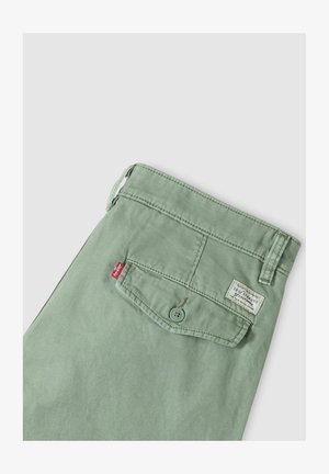 Vaaleanvihreät Levi's-housut, joissa on napillinen takatasku, punainen Levi's-merkkilappu ja valkoinen Levi Strauss -brändilaatta taskun yläpuolella.