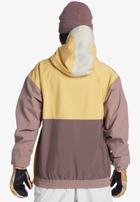 Farvet blokjakke med gule, pink og brune paneler, med hætte og elastiske ærmer. Udstyret med mønstrede handsker for ekstra stil.
