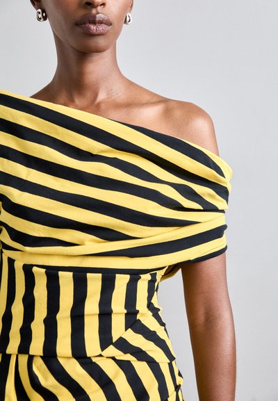 Svart- och gulrandig off-shoulder-klänning med mjuk textur och draperat tyg. Har en figurnära silhuett med lager av designinslag.