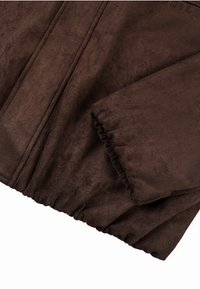 Ruda dirbtinio suede striukė, turinti susiraukšlėtą rankogalių ir apatinę kraštą. Lygus tekstūra su subtiliomis siūlų detalėmis sukuria struktūruotą išvaizdą.