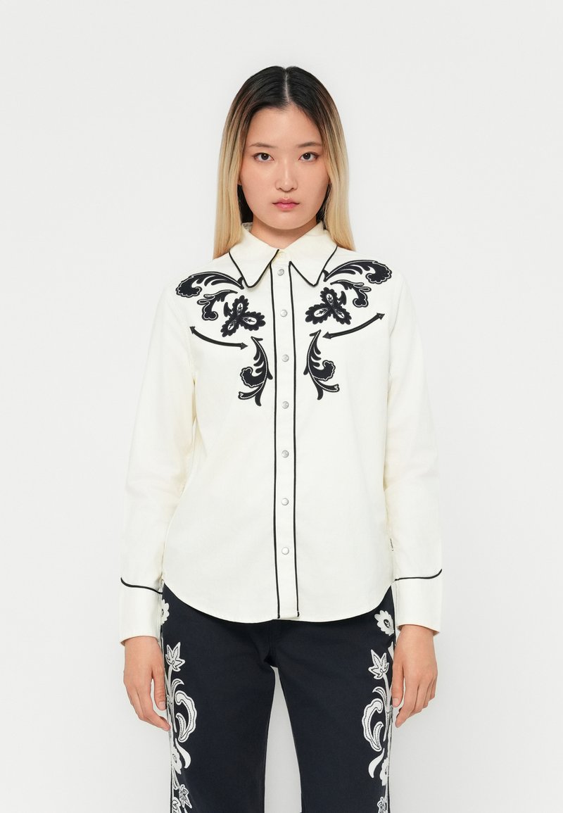 White long-sleeve shirt featuring black floral embroidery on the front and black piping along the collar and button placket.